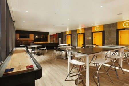 room with yellow walls, shuffleboard on side and tables with white chairs on modern bar wood flooring by Dralynn Floor Covering Inc.