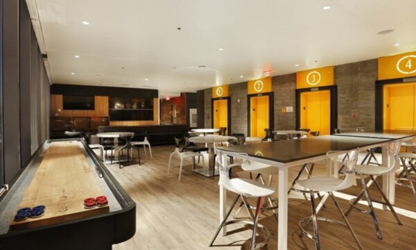 room with yellow walls, shuffleboard on side and tables with white chairs on modern bar wood flooring by Dralynn Floor Covering Inc.