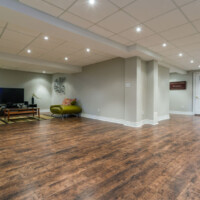 View of Open Basement with grey walls and white trim, tv on wall and Lime Green Furniture on new wooden flooring by Dralynn Floor Covering Inc.